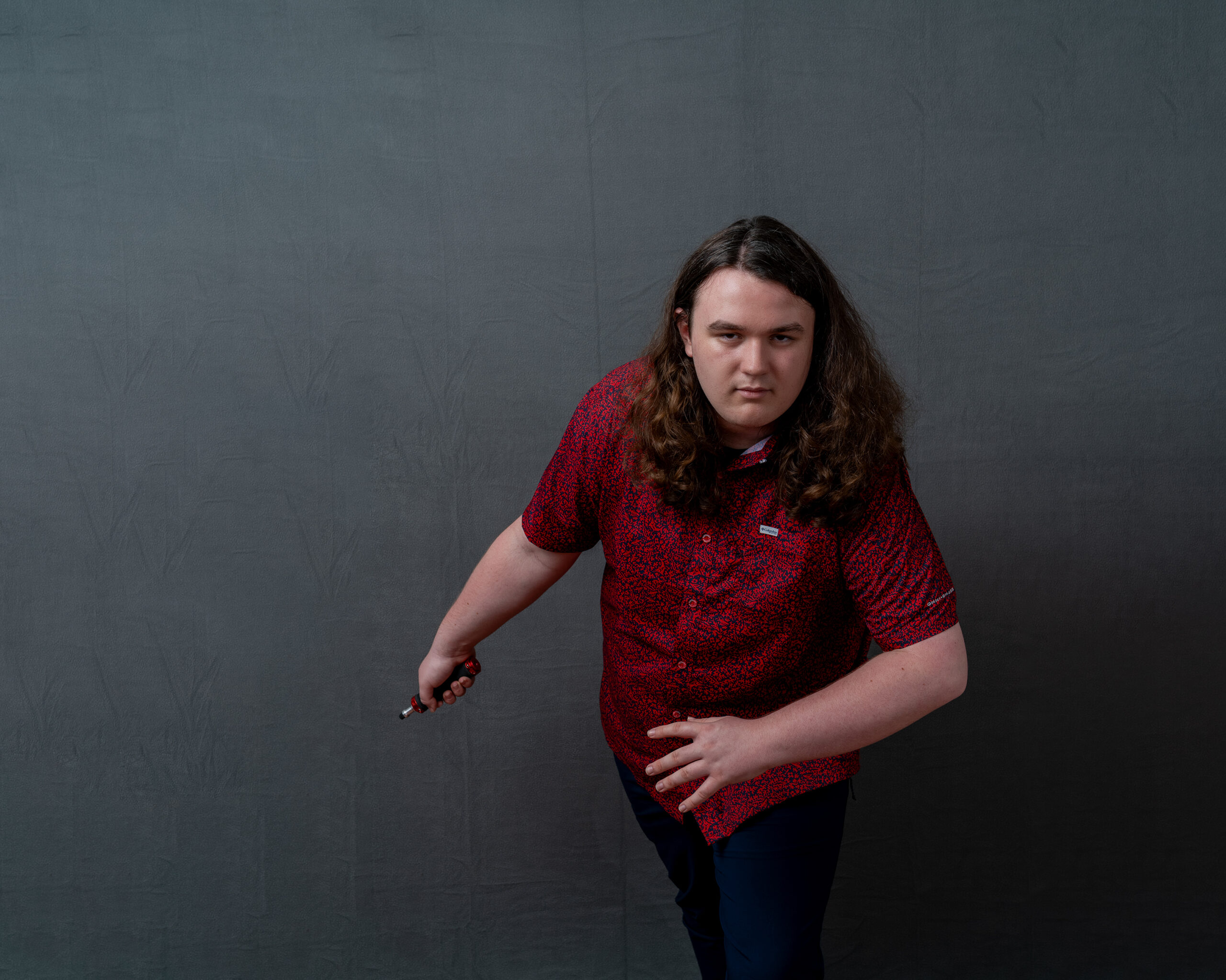 A senior in a red shirt, photographed as shot on the studio's plain gray screen.