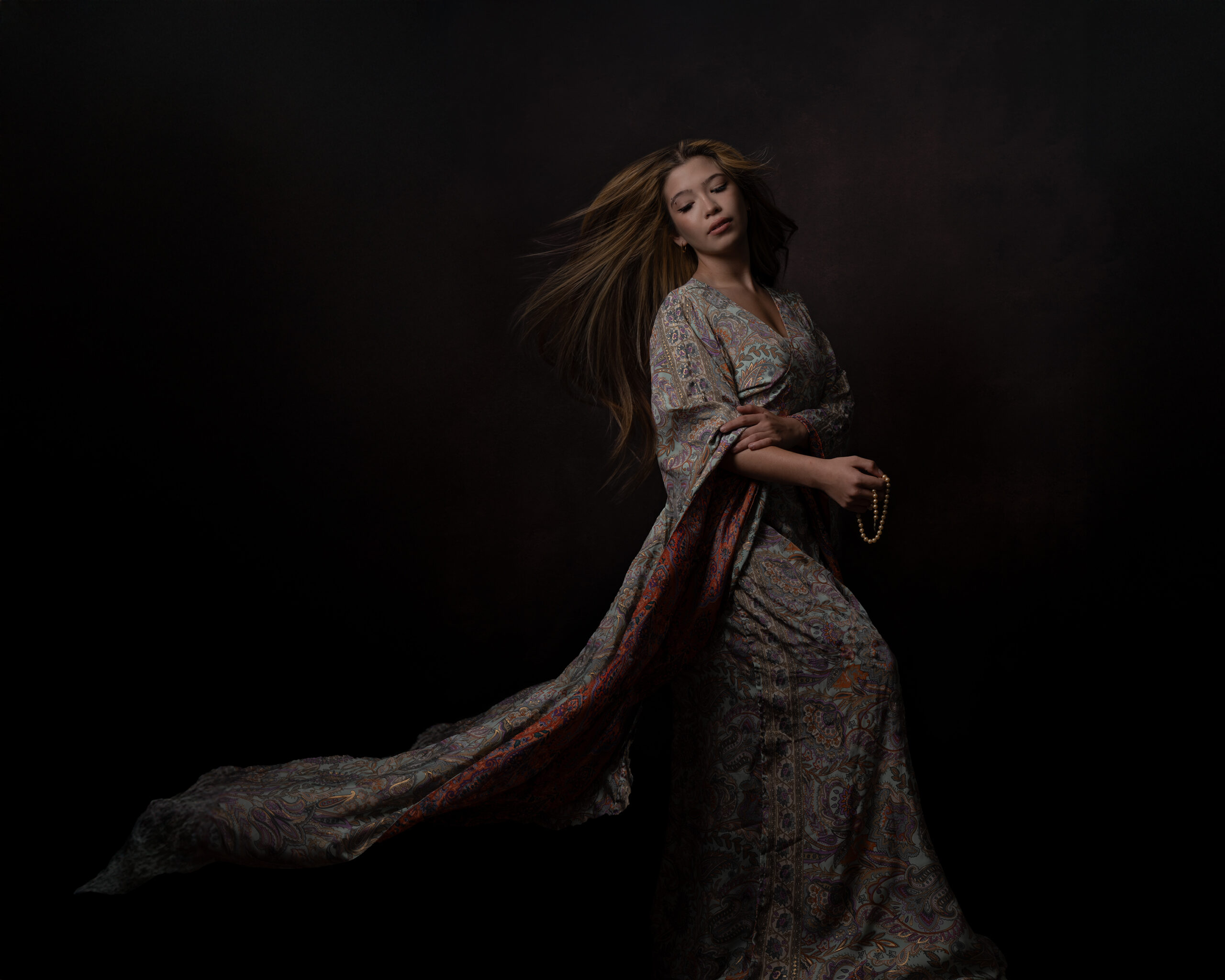 A senior in a flowing patterned gown, photographed as shot on the studio's dark backdrop.